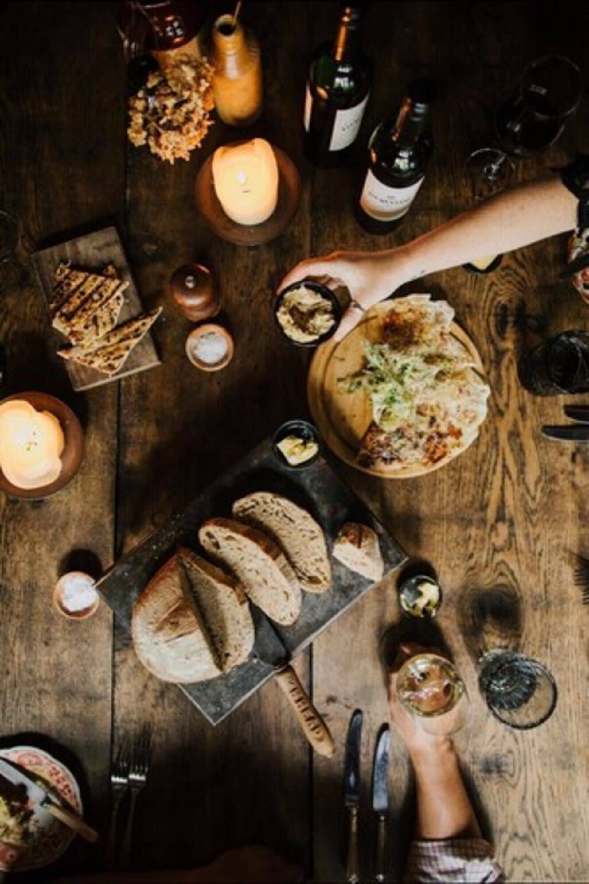 A wooden table with bread, a candle, and wine bottles.
