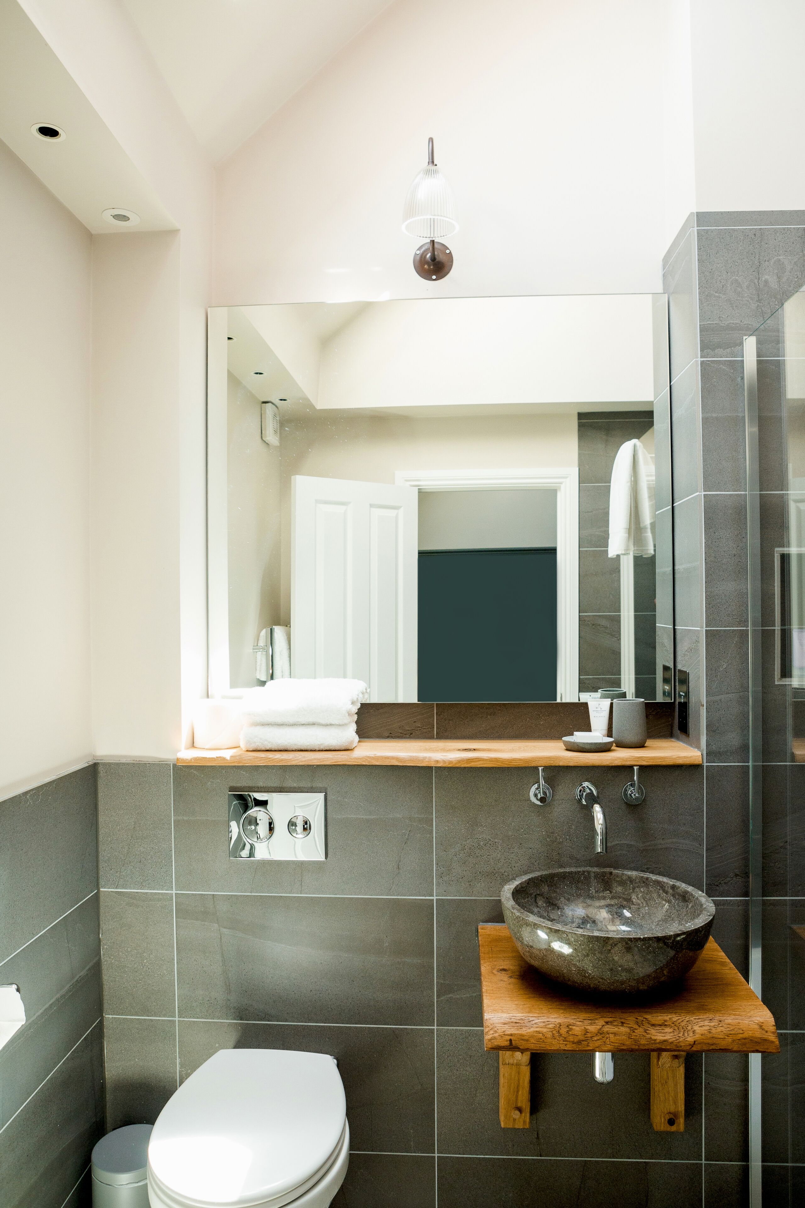 A modern bathroom with a wooden vanity, a large mirror, a vessel sink, and a toilet.