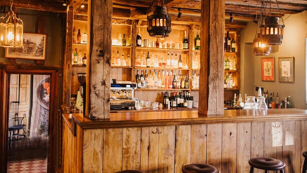 Un rústico espacio de bar con vigas de madera, barra y taburetes.