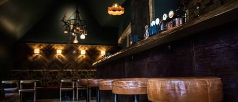 A bar area with wooden stools, a stone wall, and hanging pendant lights.