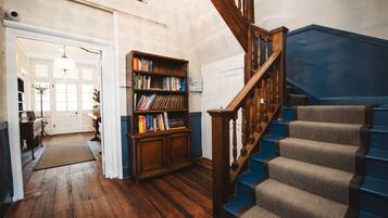 Een houten trap met blauwe treden die uitkomt op een plateau, een houten boekenkast vol boeken, en een witte deur op de achtergrond.
