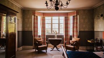 A room with a bed, two armchairs, a table, a chandelier, a window with curtains, and a radiator.