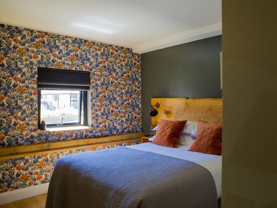 A bedroom with a floral wallpaper, a wooden headboard, and a window with a view.