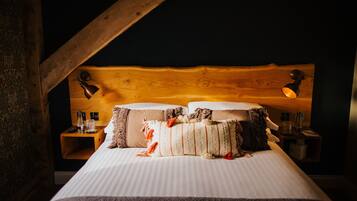 Una cama con cabecera de madera, dos lámparas de noche y una mesita de noche con una botella y vasos.
