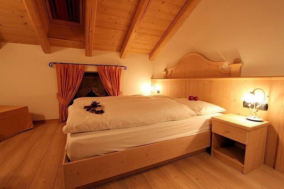 A wooden bedroom with a bed, nightstand, and curtains.