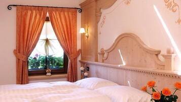 A bedroom with a wooden bed, a window with curtains, a nightstand with a vase of flowers, and a decorative headboard.