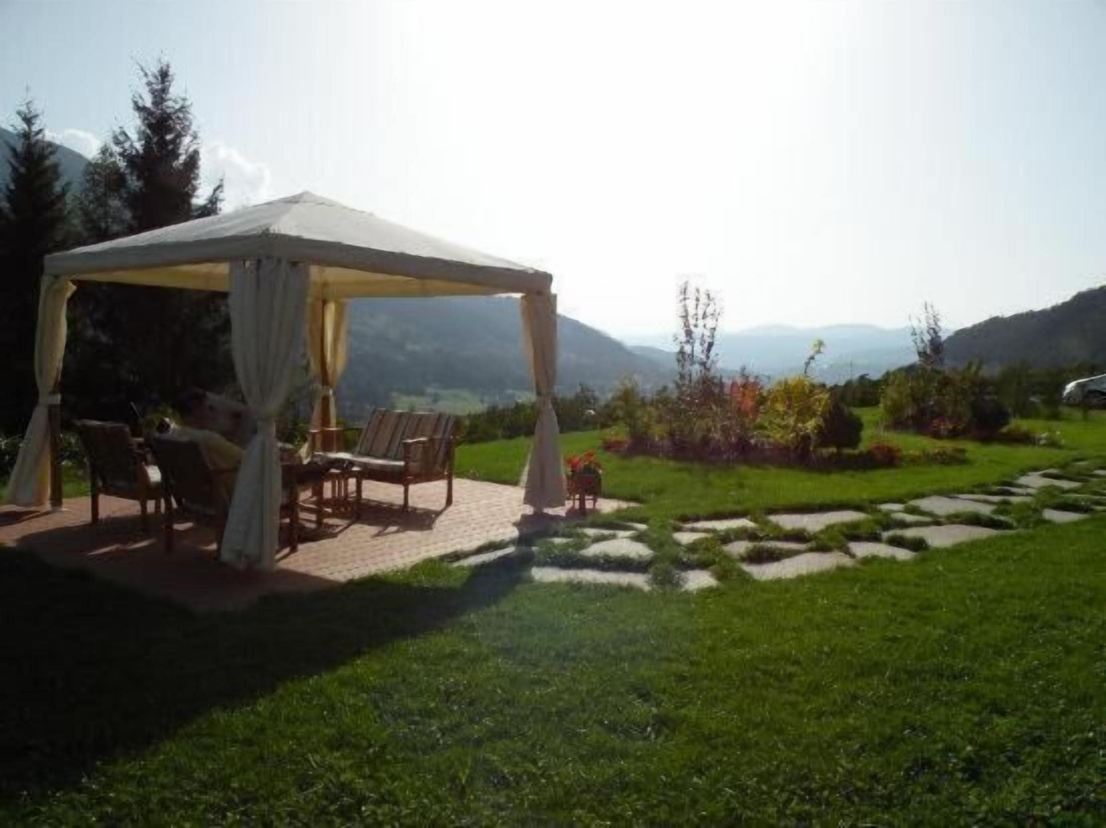 Un espace extérieur aménagé, abrité et doté de chaises et d’une table, entouré d’un jardin paysager et offrant une vue sur les montagnes lointaines.