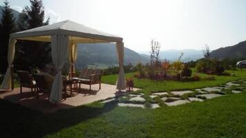 Un espace extérieur aménagé, abrité et doté de chaises et d’une table, entouré d’un jardin paysager et offrant une vue sur les montagnes lointaines.