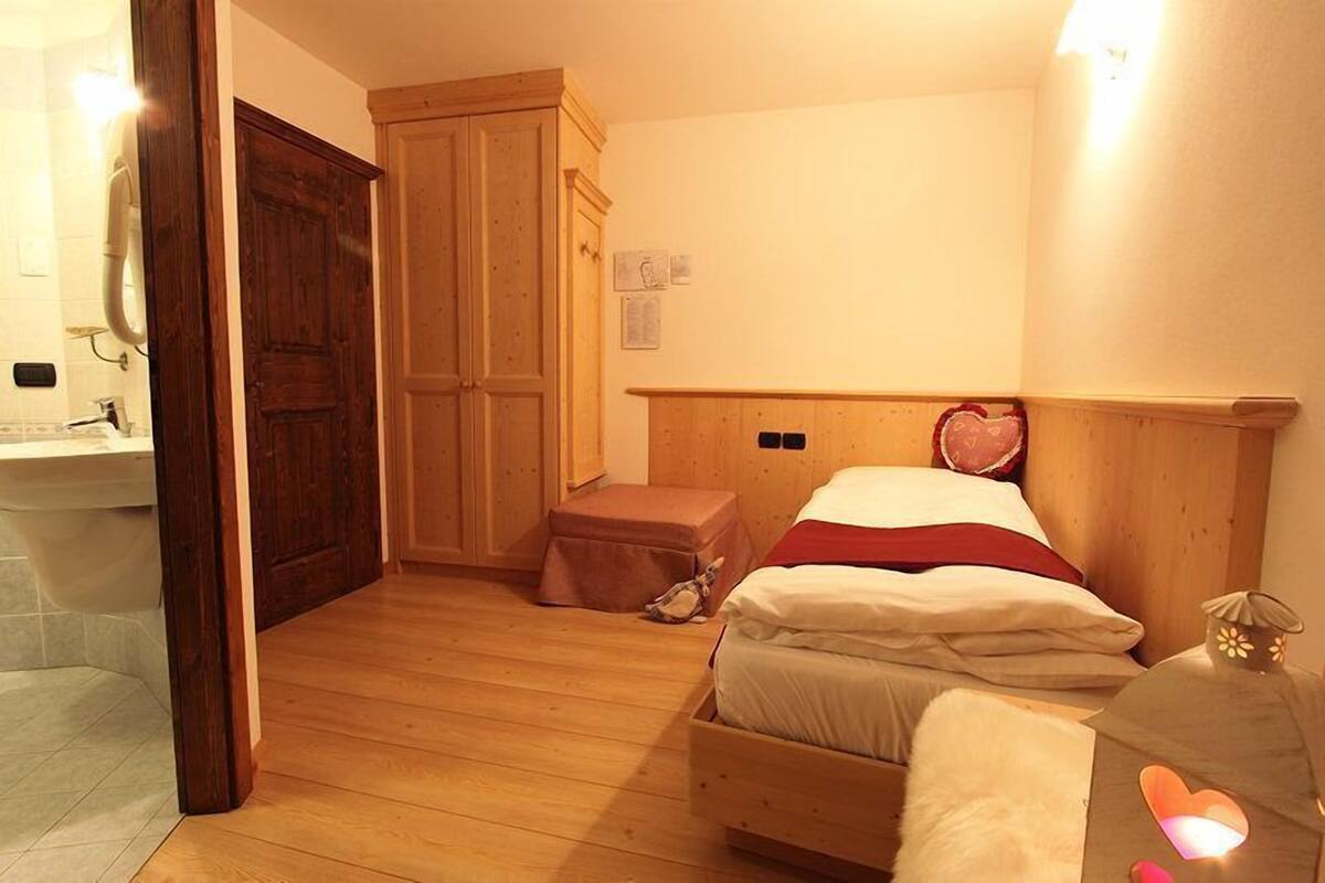 A bedroom with a wooden bed, a nightstand, a wooden wardrobe, and a small stool.