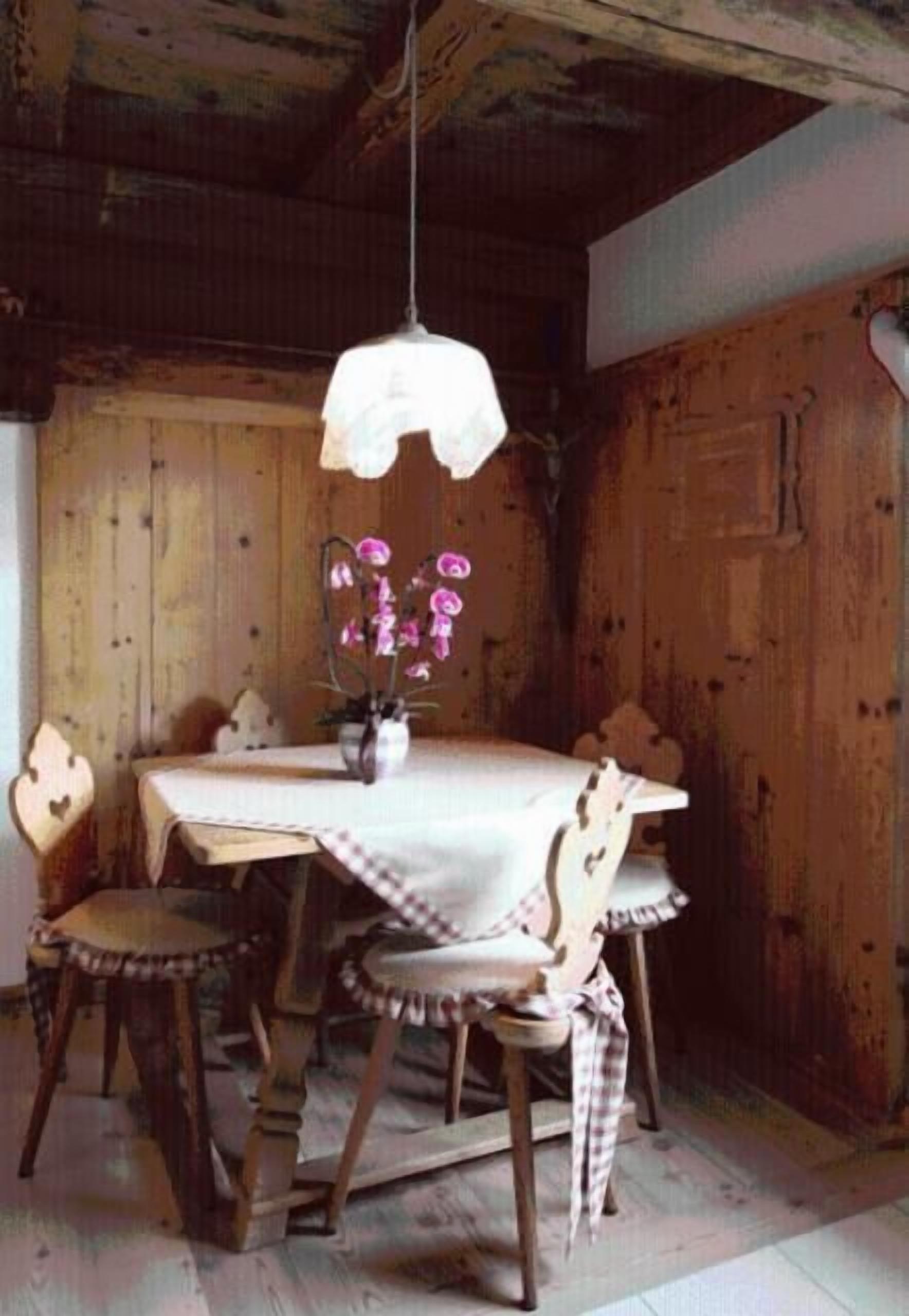 A rustic wooden dining room with a table set for four, surrounded by wooden chairs with plaid cushions.