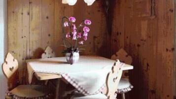 A rustic wooden dining room with a table set for four, surrounded by wooden chairs with plaid cushions.