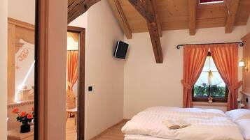 Un dormitorio con techo de madera, cama con ropa blanca, televisor montado en la pared y ventana con cortinas.