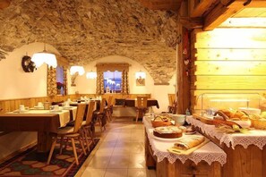 A rustic dining area with wooden tables and chairs, stone walls, and a view through an arched window. - Hotel Garni Fonte dei Veli (Panchia)
