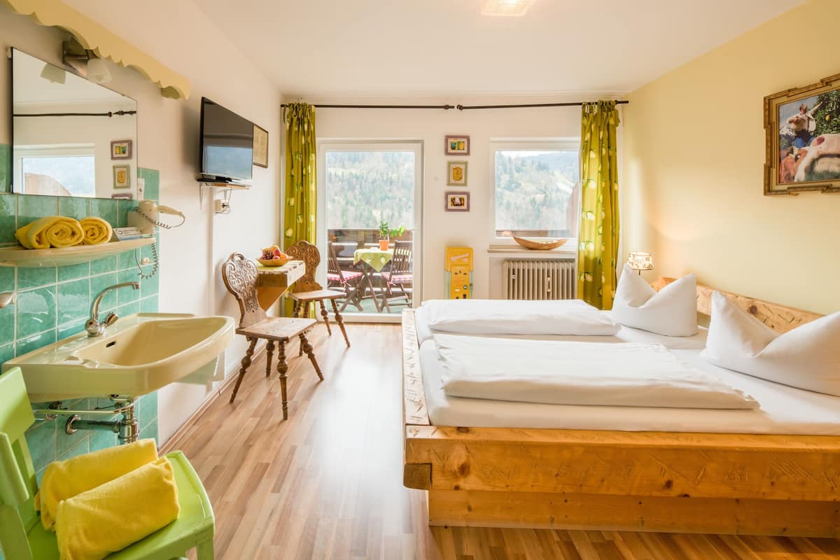 Ein Hotelzimmer mit einem hölzernen Bett, einem grünen Stuhl, einem Waschbecken und einem Balkon mit Bergblick.