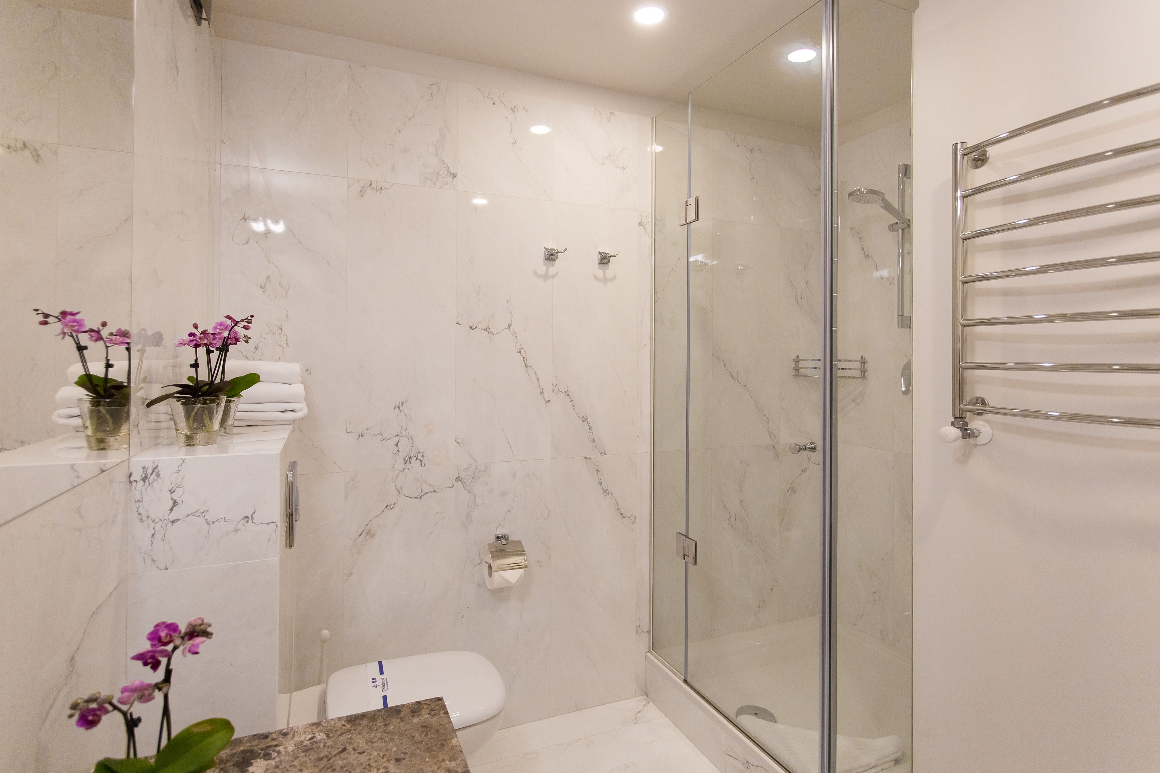 Un baño moderno con ducha acristalada, paredes de mármol y puerta de vidrio.