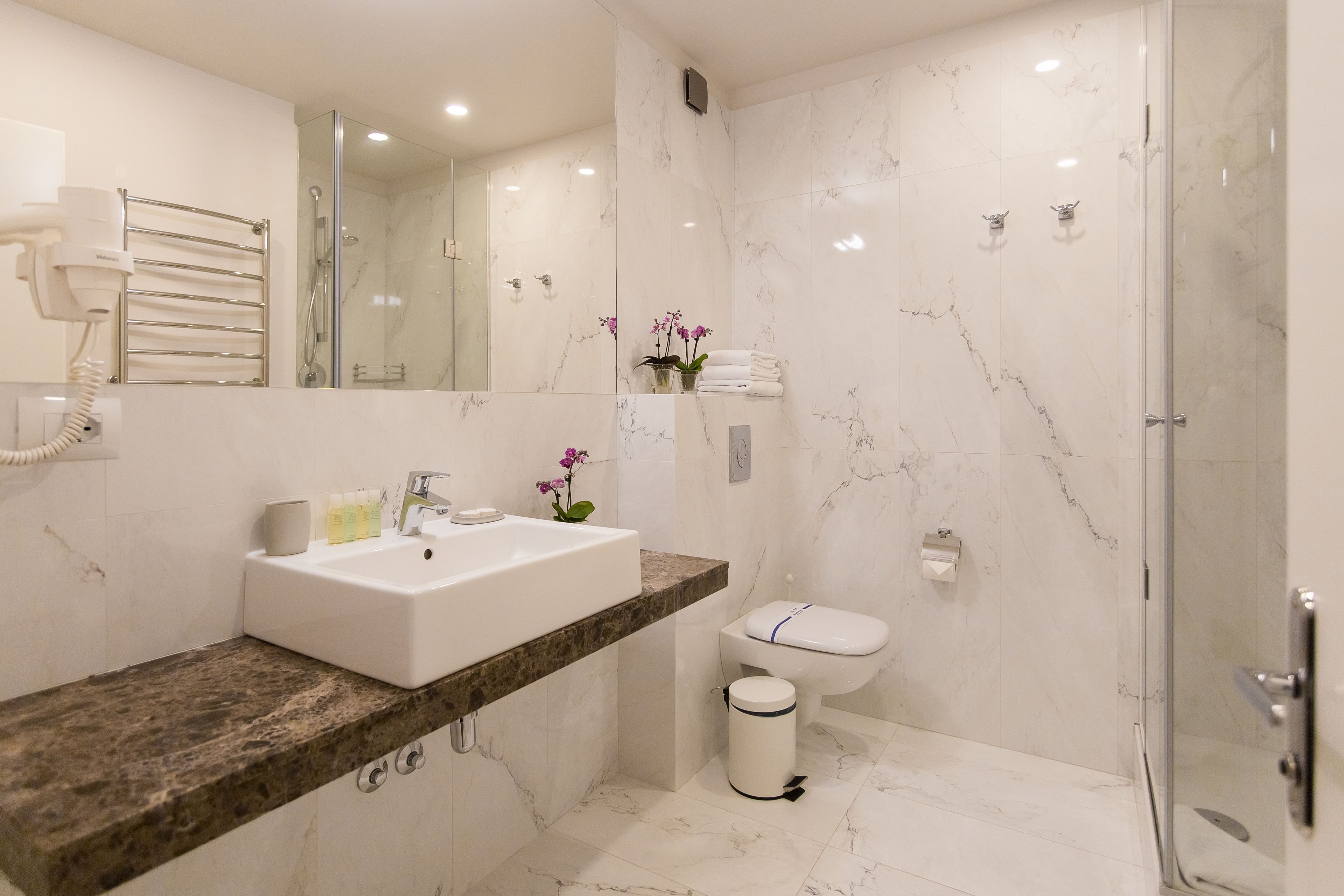 Un baño moderno con lavamanos de mármol, ducha con mampara de vidrio y un inodoro.
