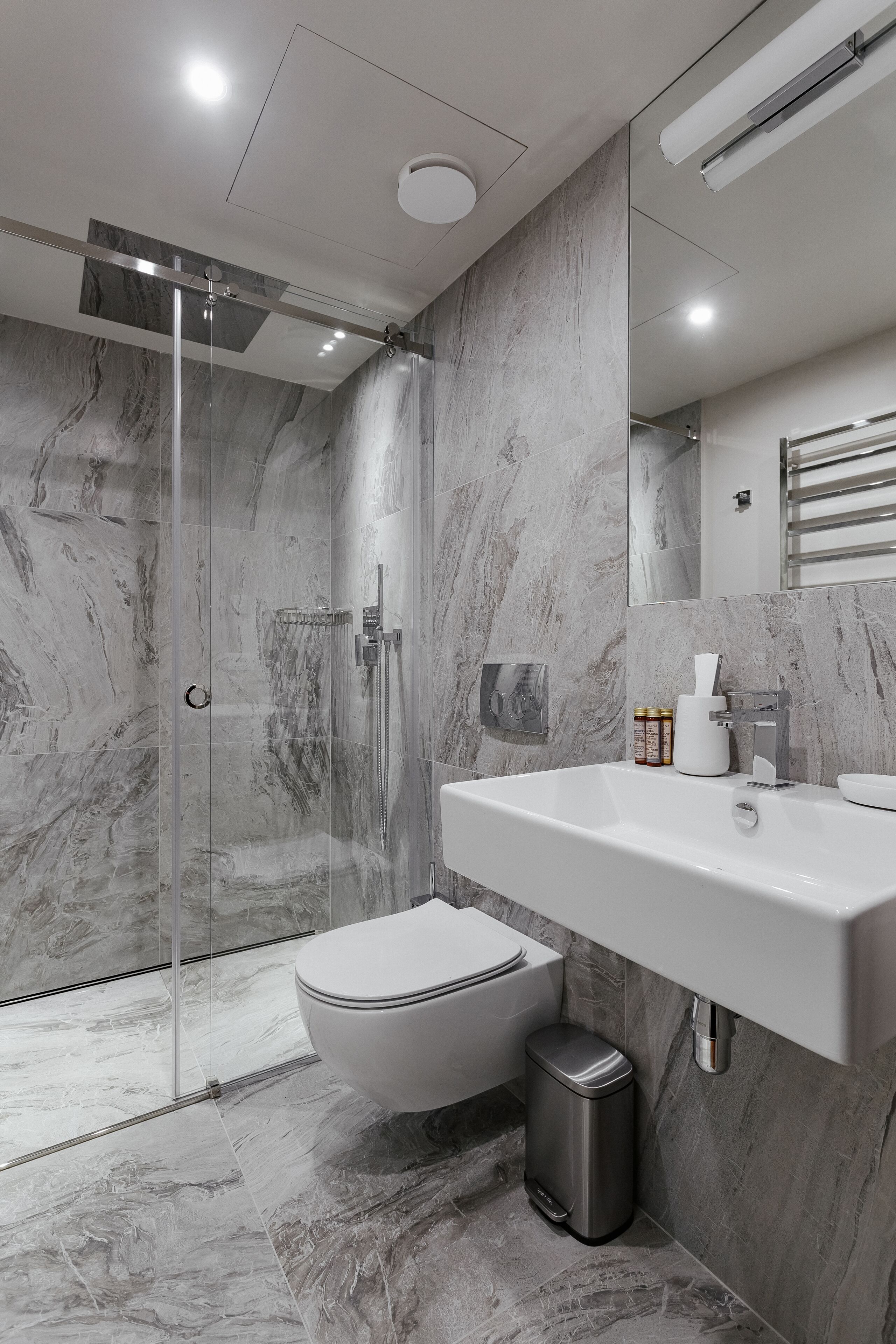 Un baño moderno con ducha de vidrio, inodoro blanco y piso de mármol.