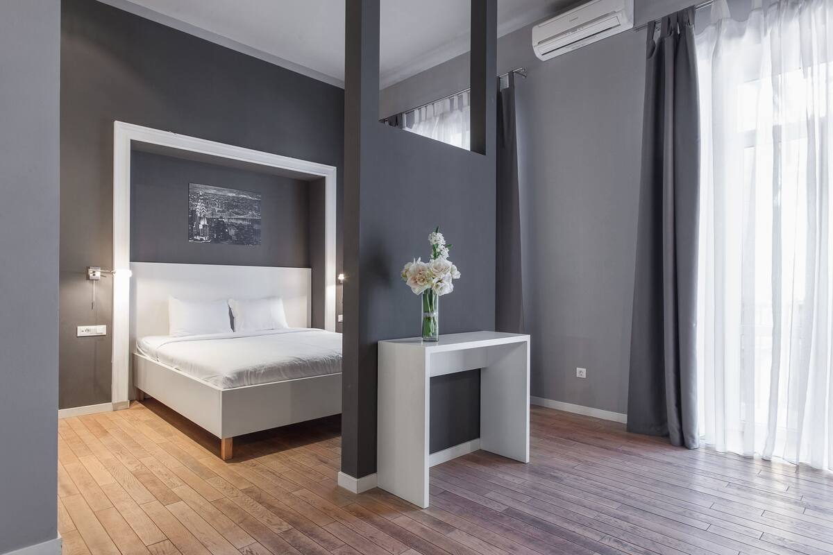 A modern bedroom with a bed, a bedside table, a wall-mounted air conditioner, and a window with curtains.
