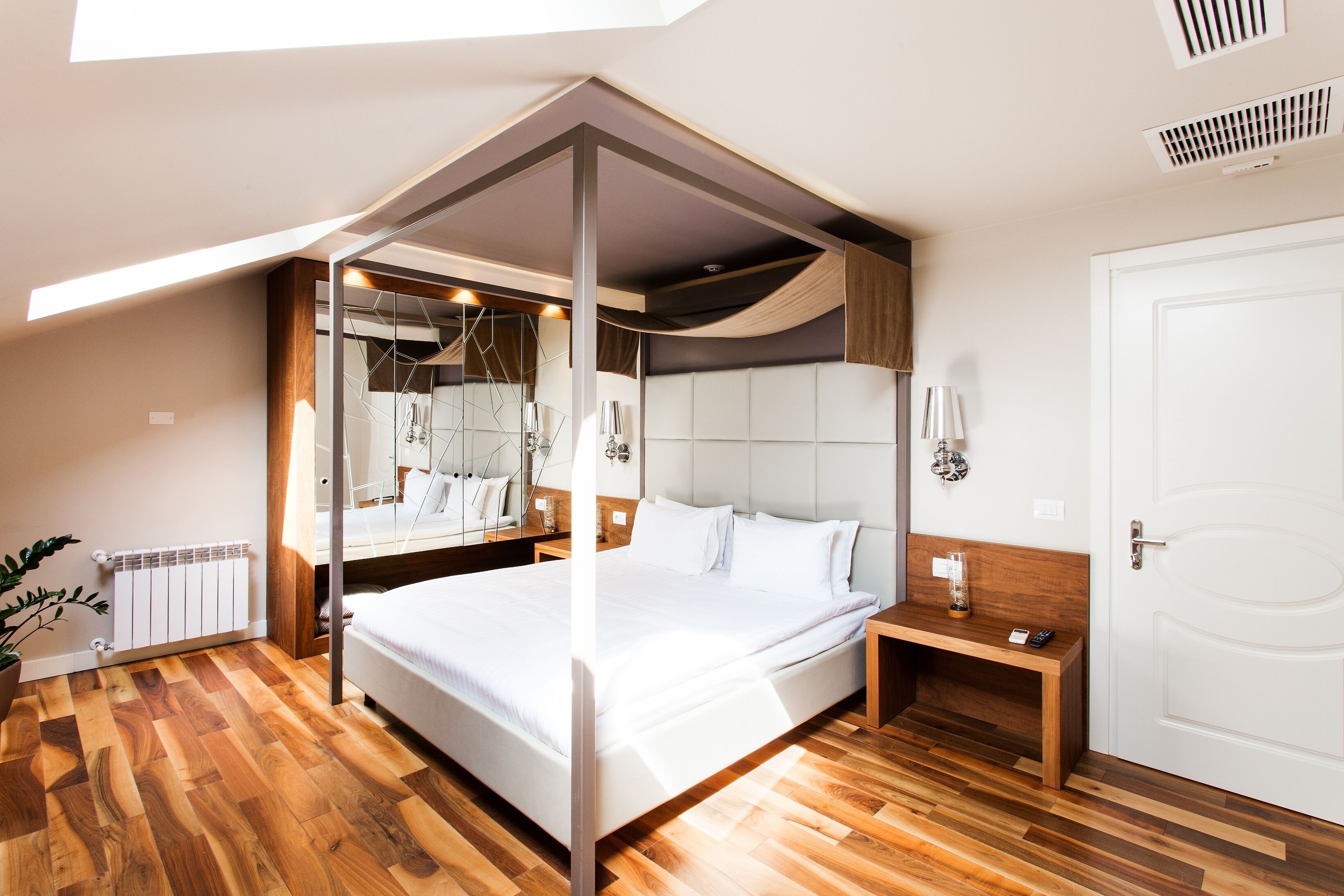 A modern bedroom with a large bed, a bedside table, a nightstand, a mirror, and a radiator.