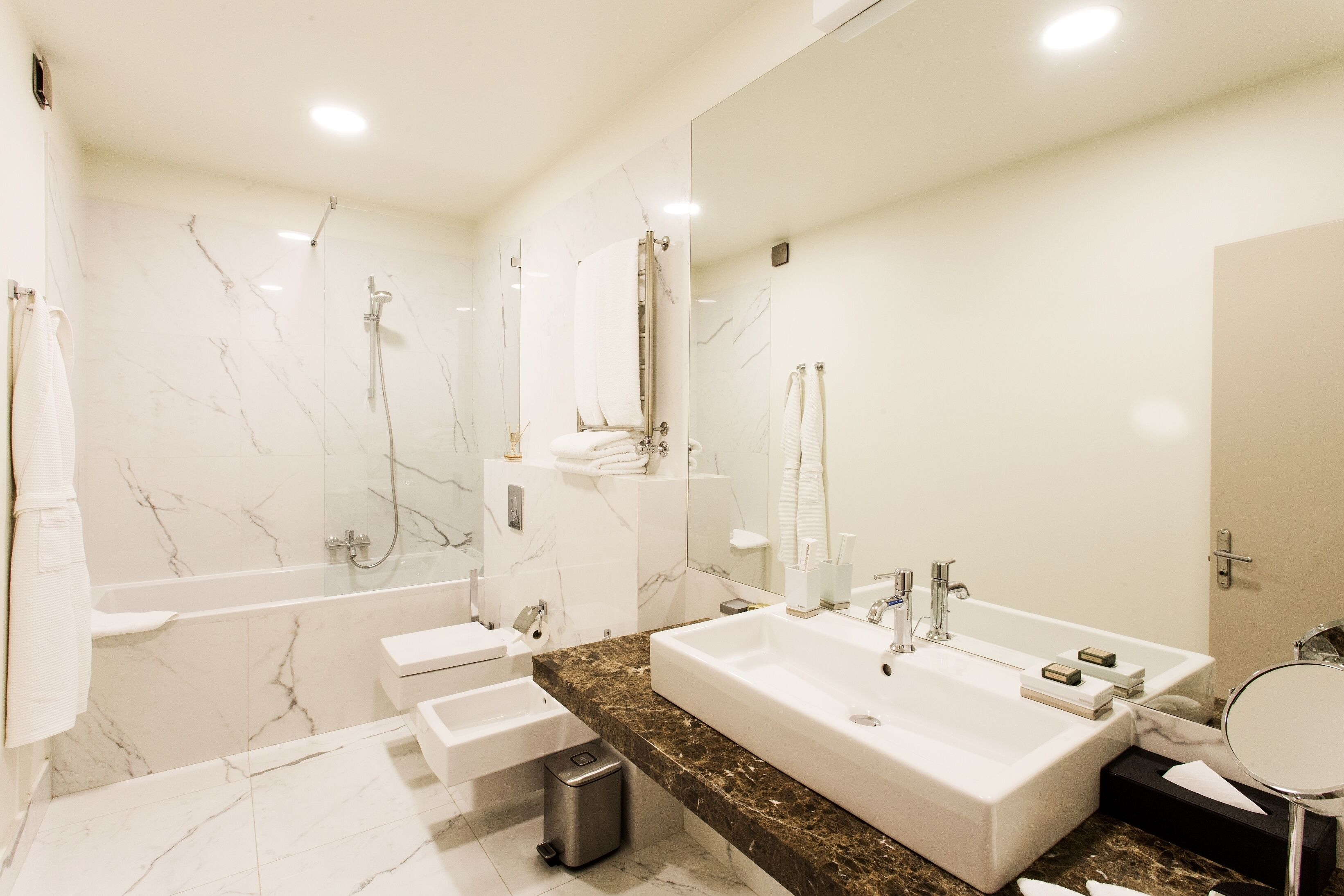 A modern bathroom with a large sink, a bathtub, and a shower. There are towels and toiletries on the counter.
