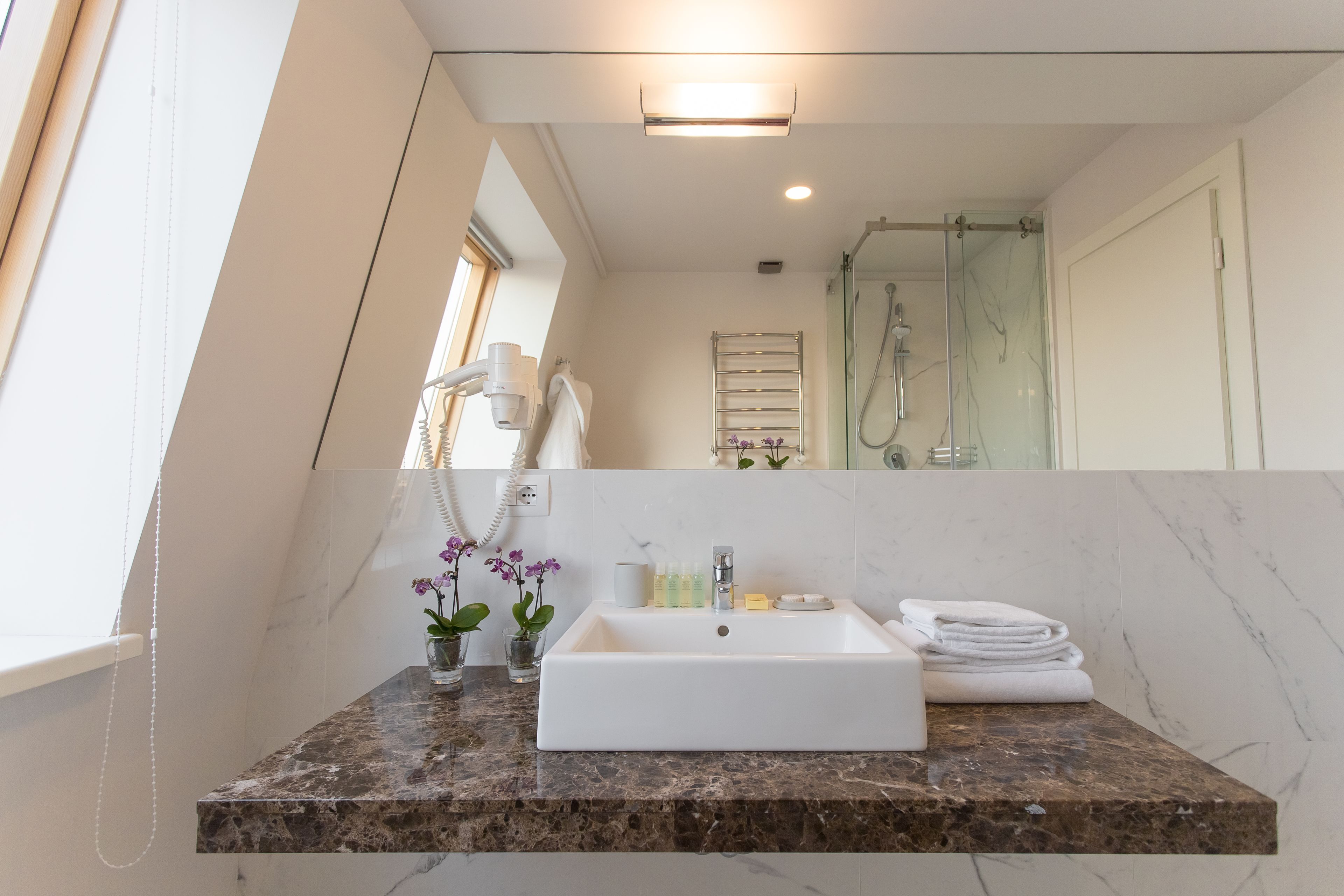 A bathroom with a marble countertop, a white sink, a glass shower enclosure, and a towel rack.