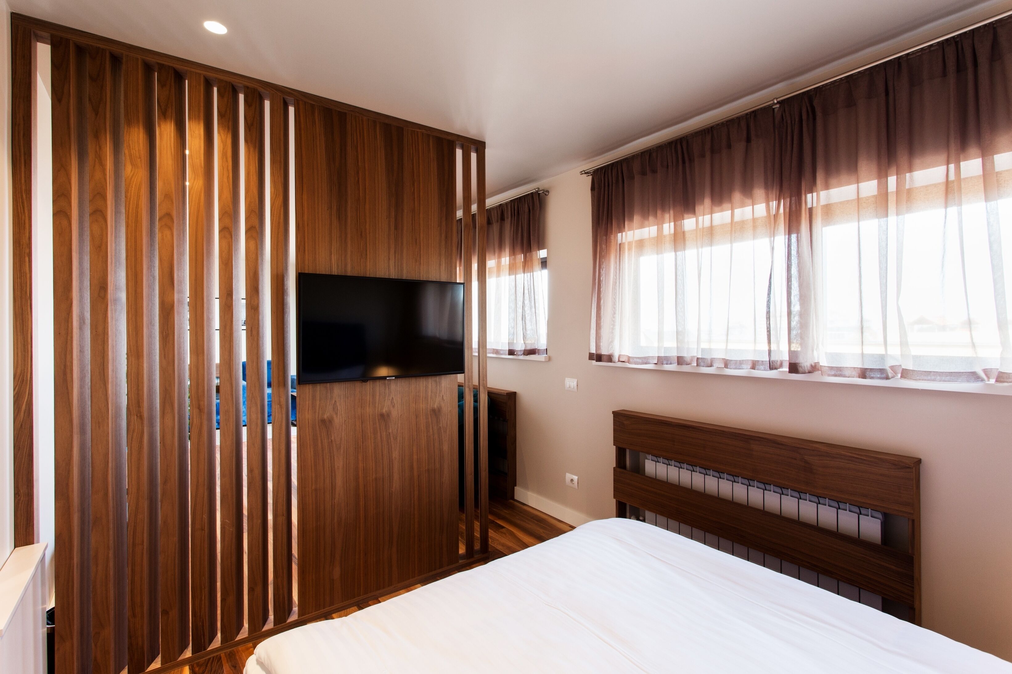 Un dormitorio con un armario de madera, un televisor de pantalla plana, una cama con cabecera de madera y una ventana con cortinas.