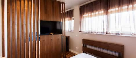 Un dormitorio con un armario de madera, un televisor de pantalla plana, una cama con cabecera de madera y una ventana con cortinas.