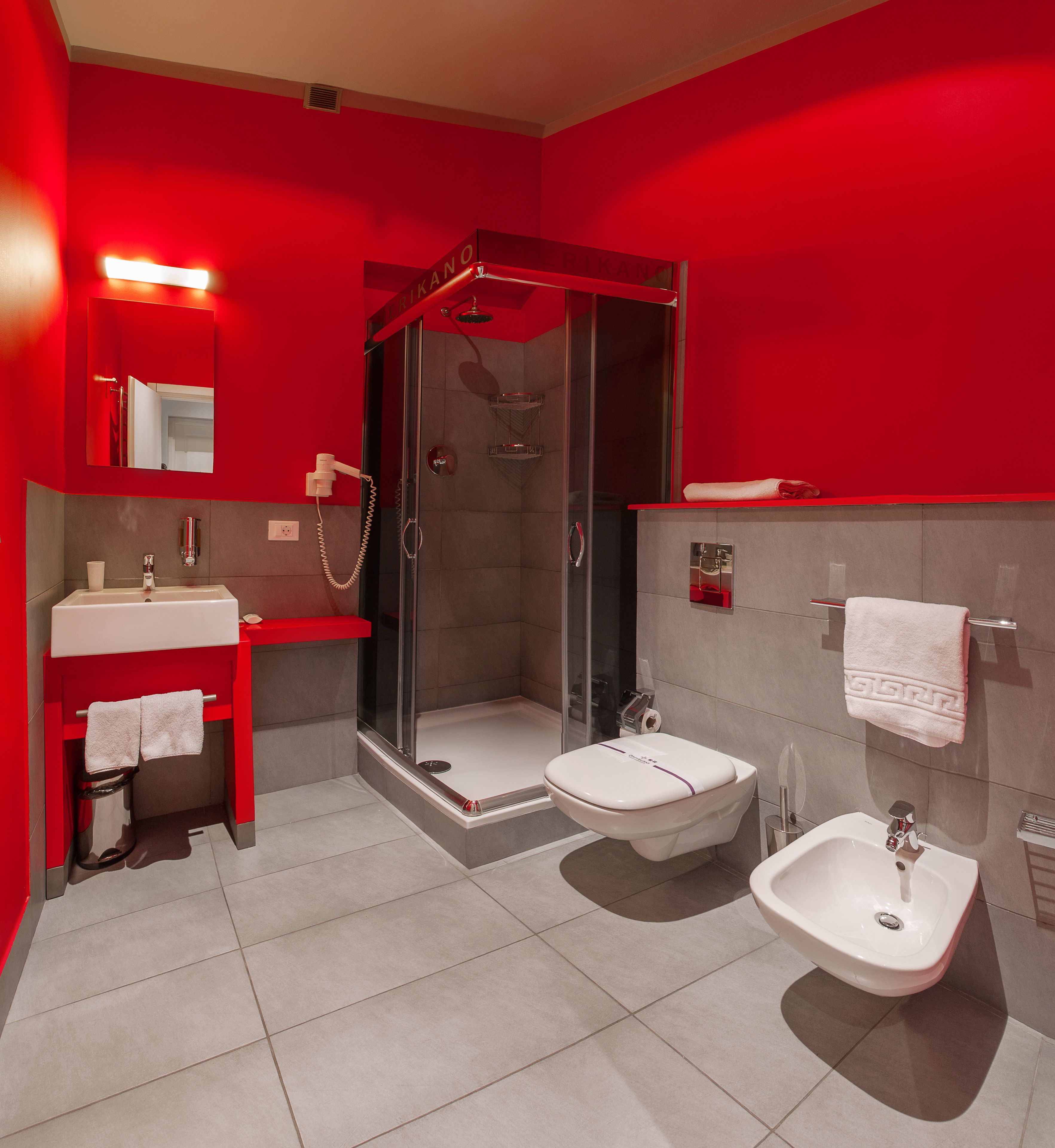 Un baño moderno con una decoración en tonos rojos, que incluye ducha, inodoro, bidé y lavamanos.