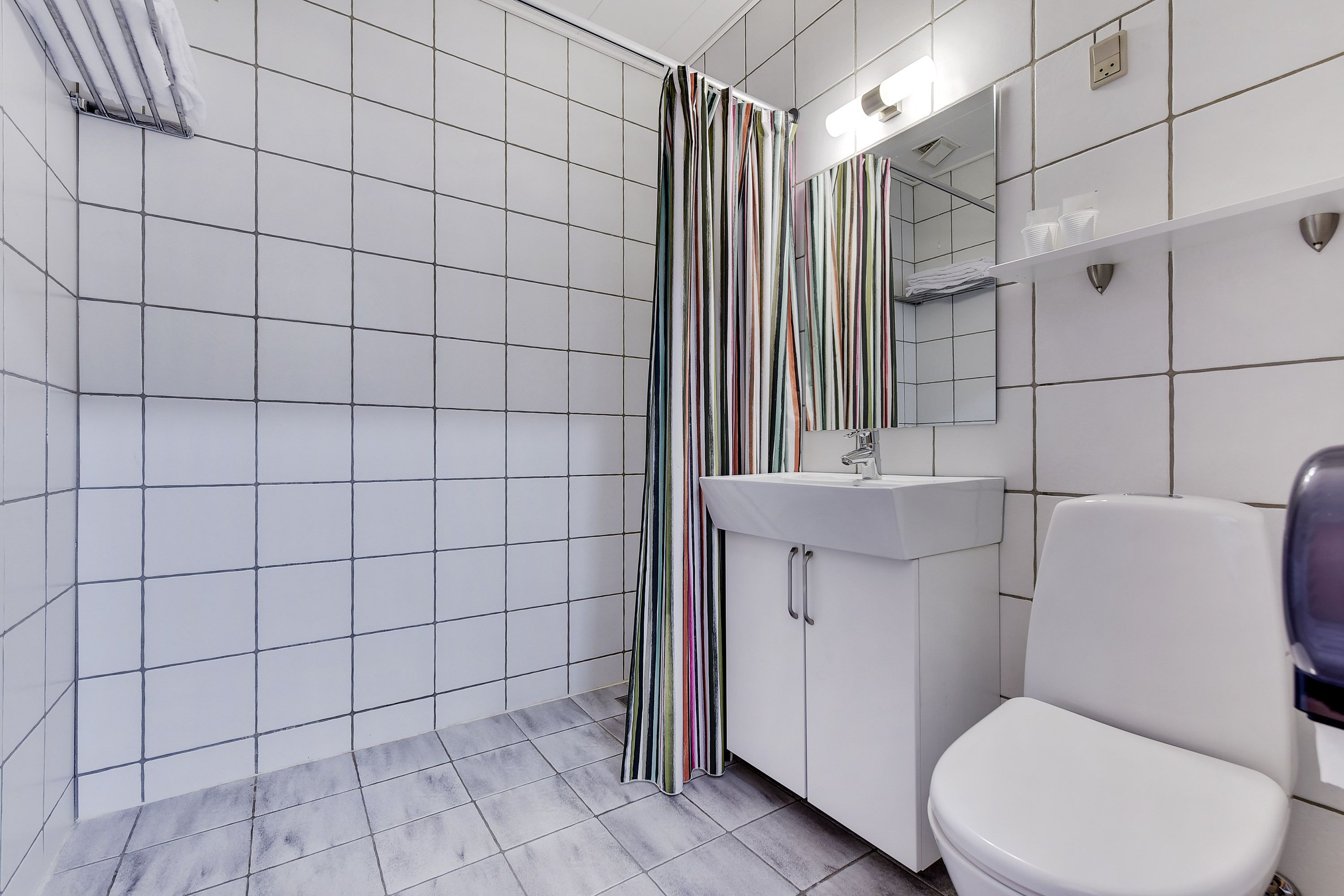 A bathroom with white tiled walls, a striped shower curtain, a white sink, and a toilet.