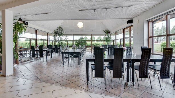 A spacious indoor dining area with multiple tables and chairs, large windows, and ceiling fans.