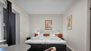A hotel room with two beds, a desk, a chair, and artwork on the walls.