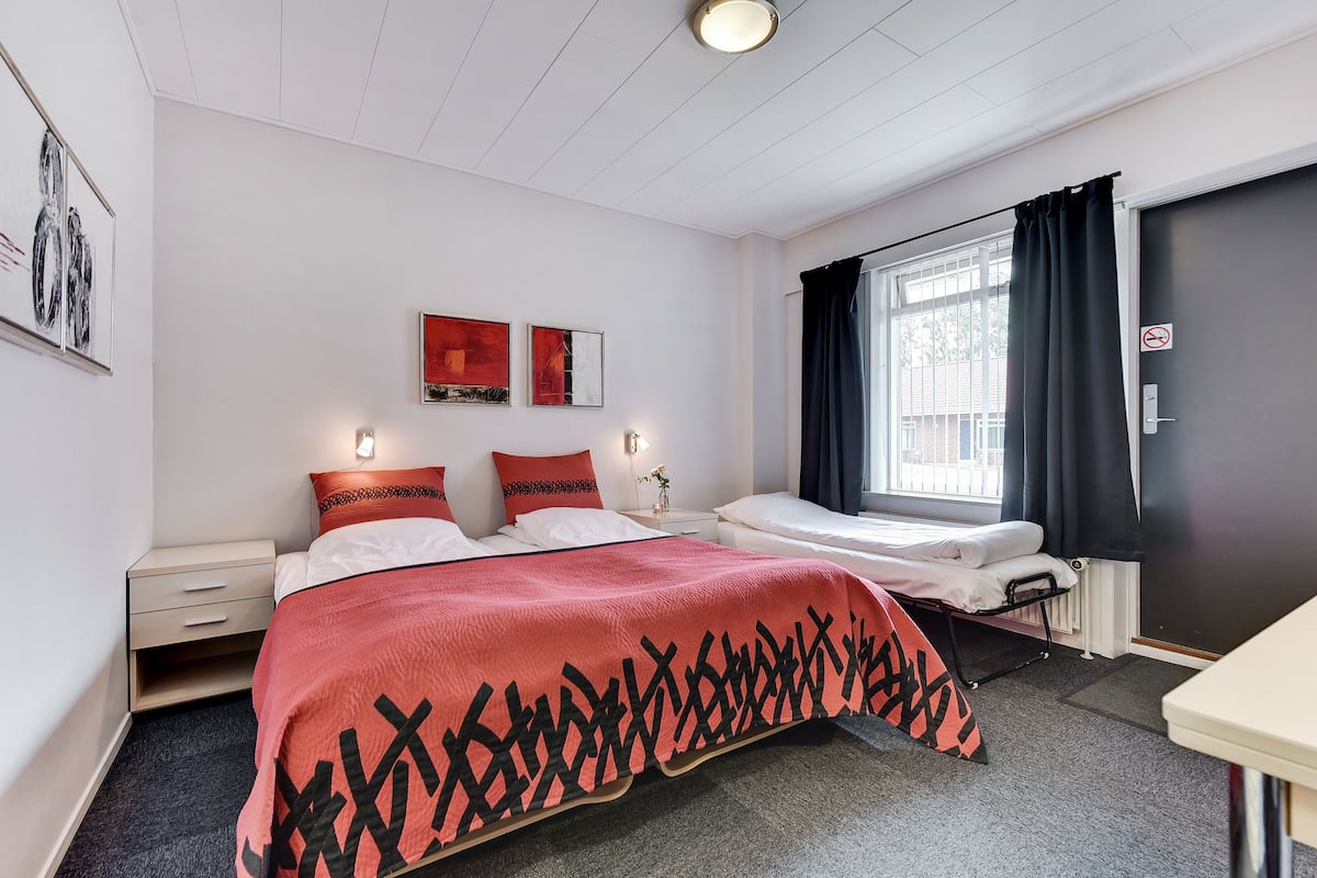 A hotel room with a bed, bedside tables, a desk, and a window with curtains.