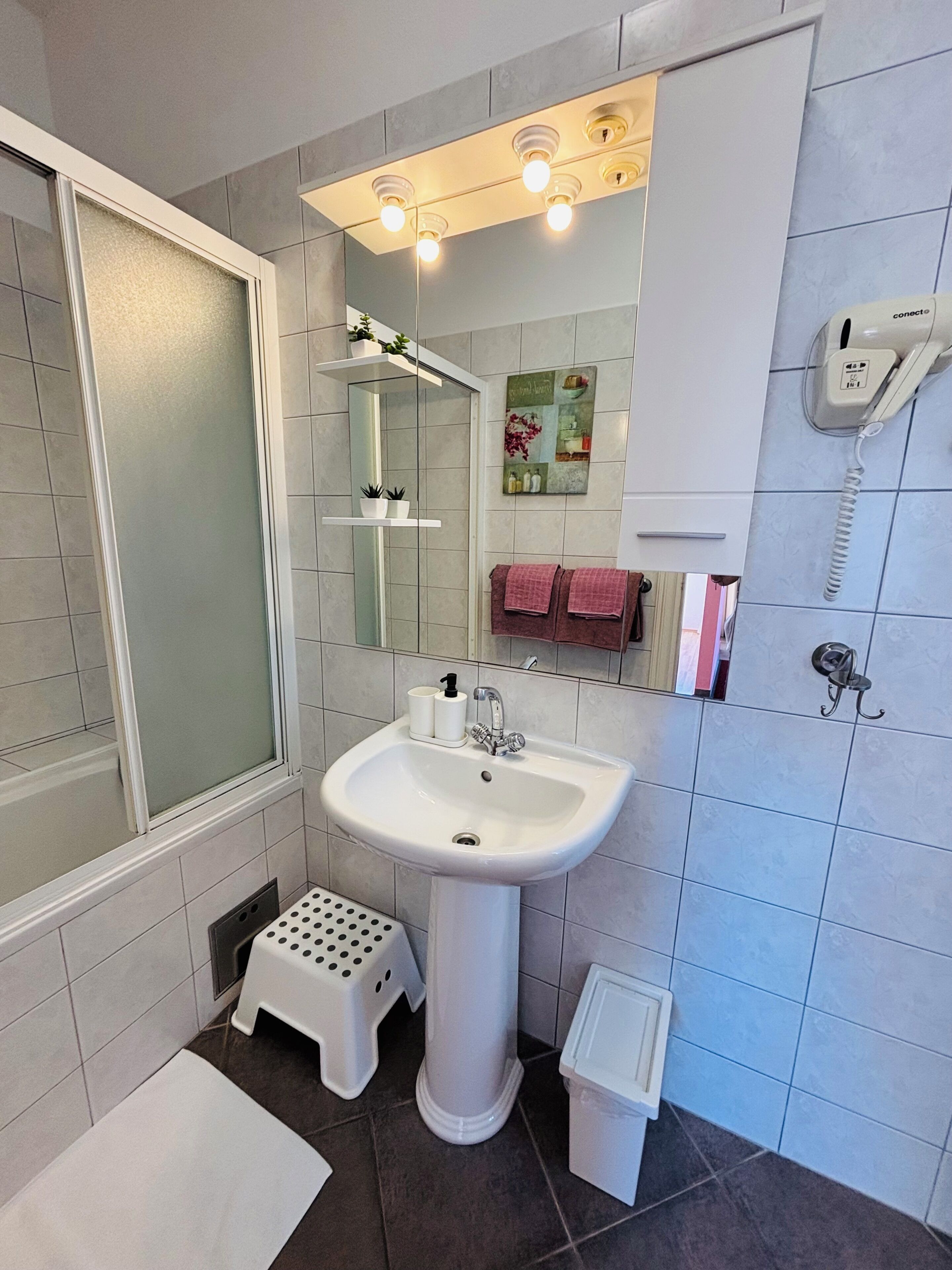 Une salle de bain avec un lavabo blanc, une douche, des toilettes et un téléphone.