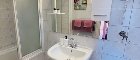 A bathroom with a white sink, a shower, a toilet, and a telephone.