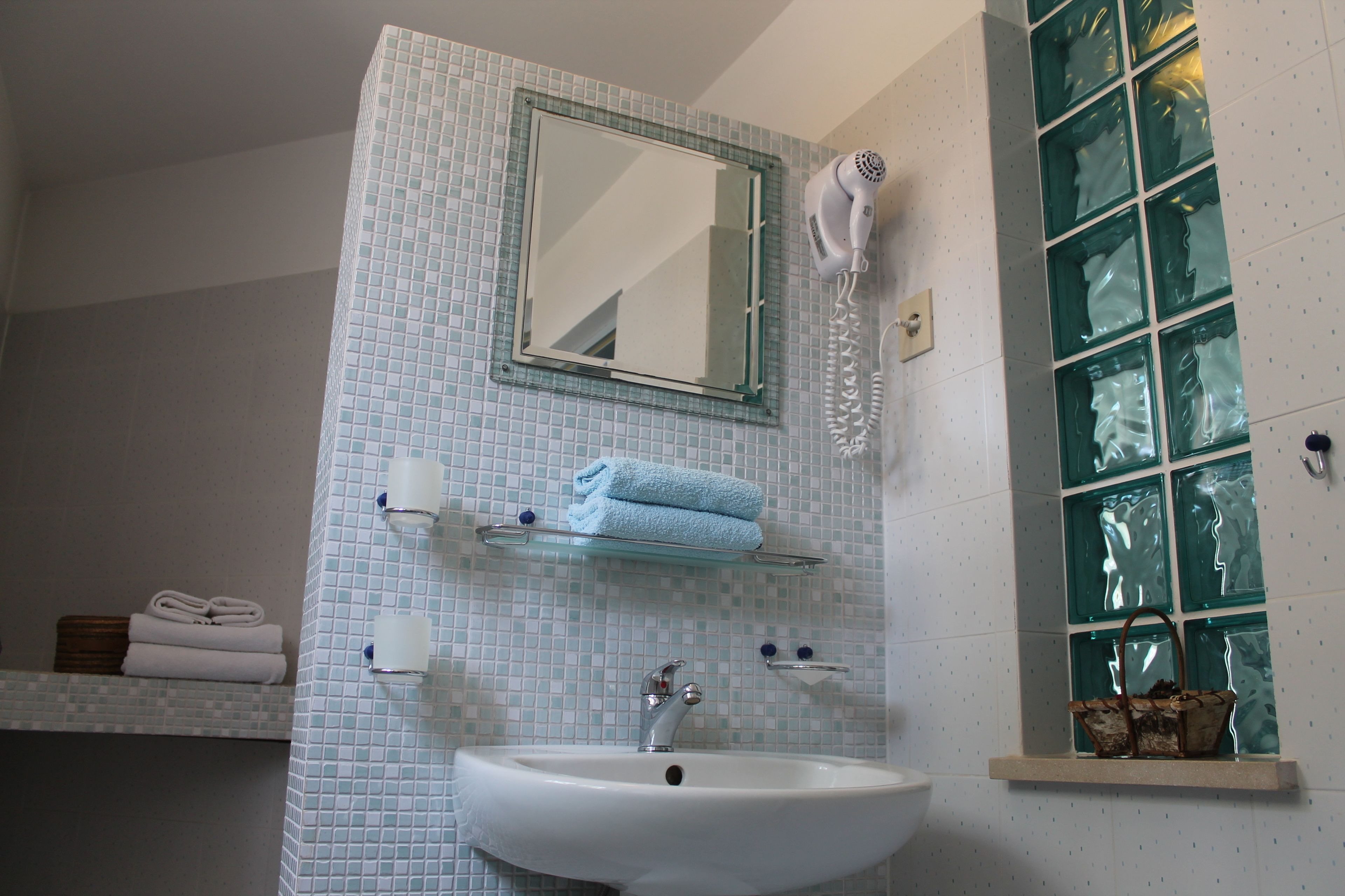 A bathroom with a white sink, a mirror, a hairdryer, and a window with green glass panes.