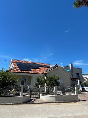 A house with a red-tiled roof, solar panels, a gated entrance, and a clear blue sky. - Villa Mandolina Apartments (Zadar)