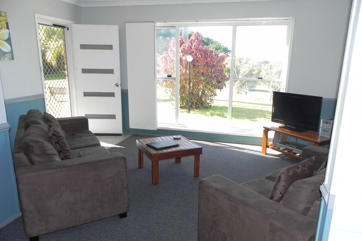 A living room with two sofas, a coffee table, a TV, and a sliding glass door leading to a garden.