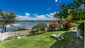 A backyard with a white fence, a lawn, and a view of a lake.