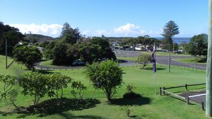 A grassy area with a flagpole, a road, and a distant view of a town with buildings and trees.