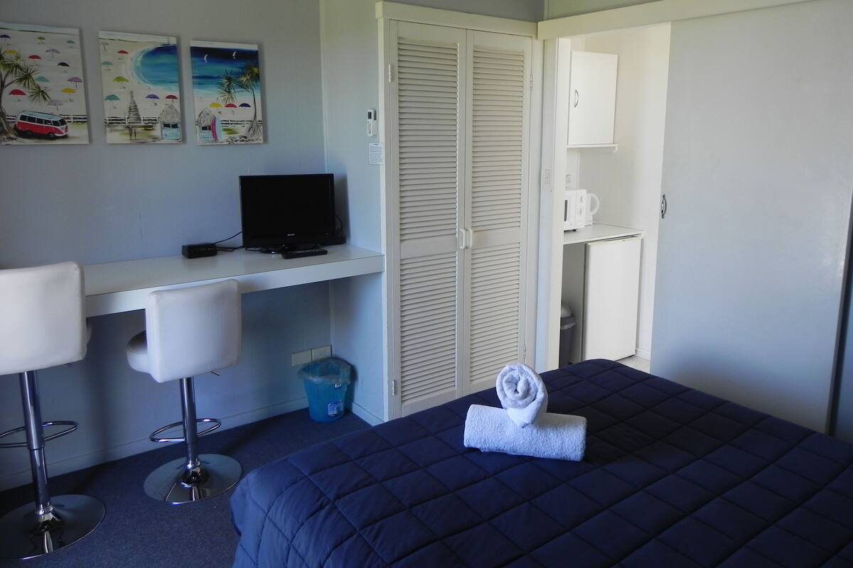 A hotel room with a bed, a desk with a computer, a chair, and a wardrobe.