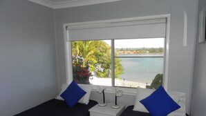 A bedroom with two beds, a nightstand, and a window with a view of a body of water and greenery.