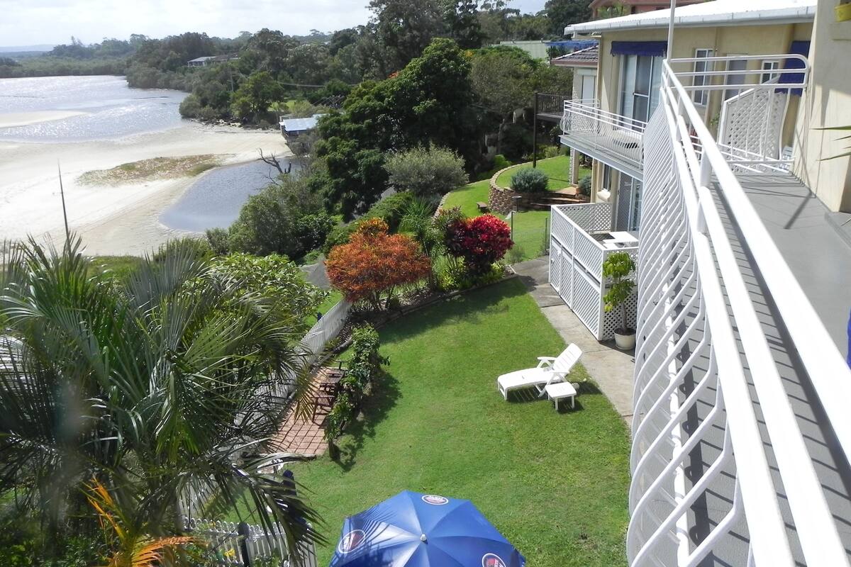 A balcony with a view of a beach and a well-maintained garden.