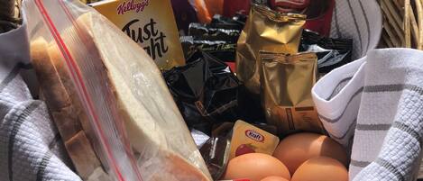 A wicker basket filled with various food items including bread, eggs, and packaged snacks.