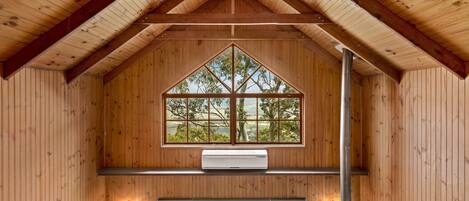 Interior de uma cabana de madeira, com uma janela grande, uma escada e uma área de estar.