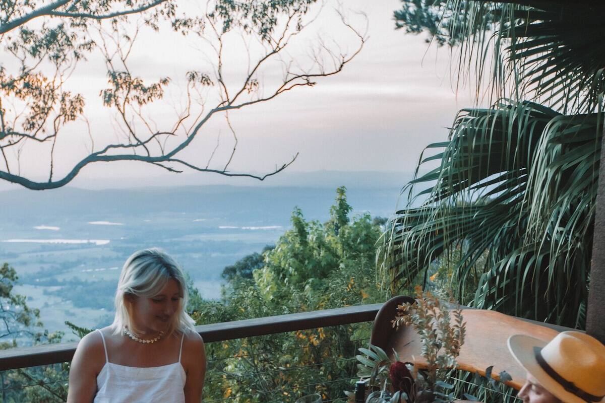 Deux personnes sont assises sur une terrasse en bois, une table les séparant, et elles ont devant elles une vue imprenable sur un paysage magnifique.