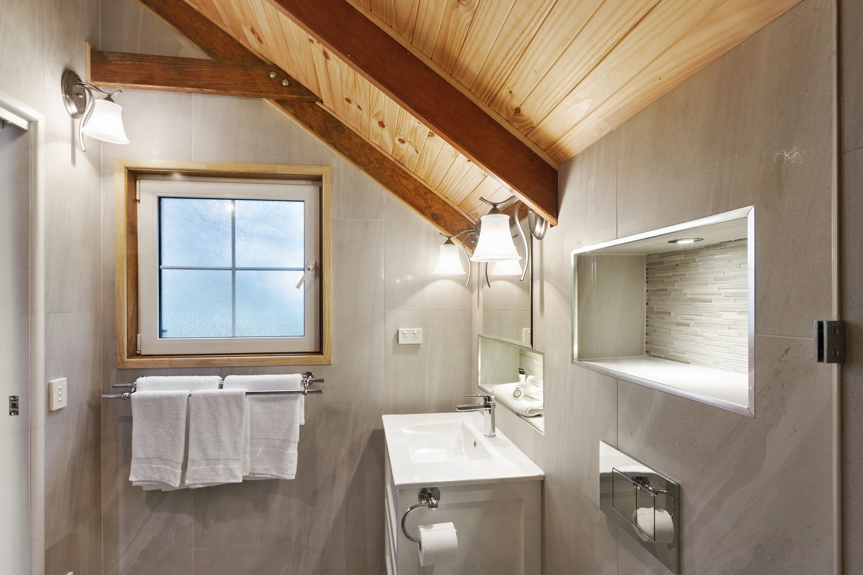 A bathroom with a wooden ceiling, a window, a sink, a mirror, and a towel rack.