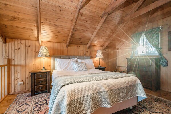 A wooden cabin bedroom with a bed, two nightstands, and a dresser.