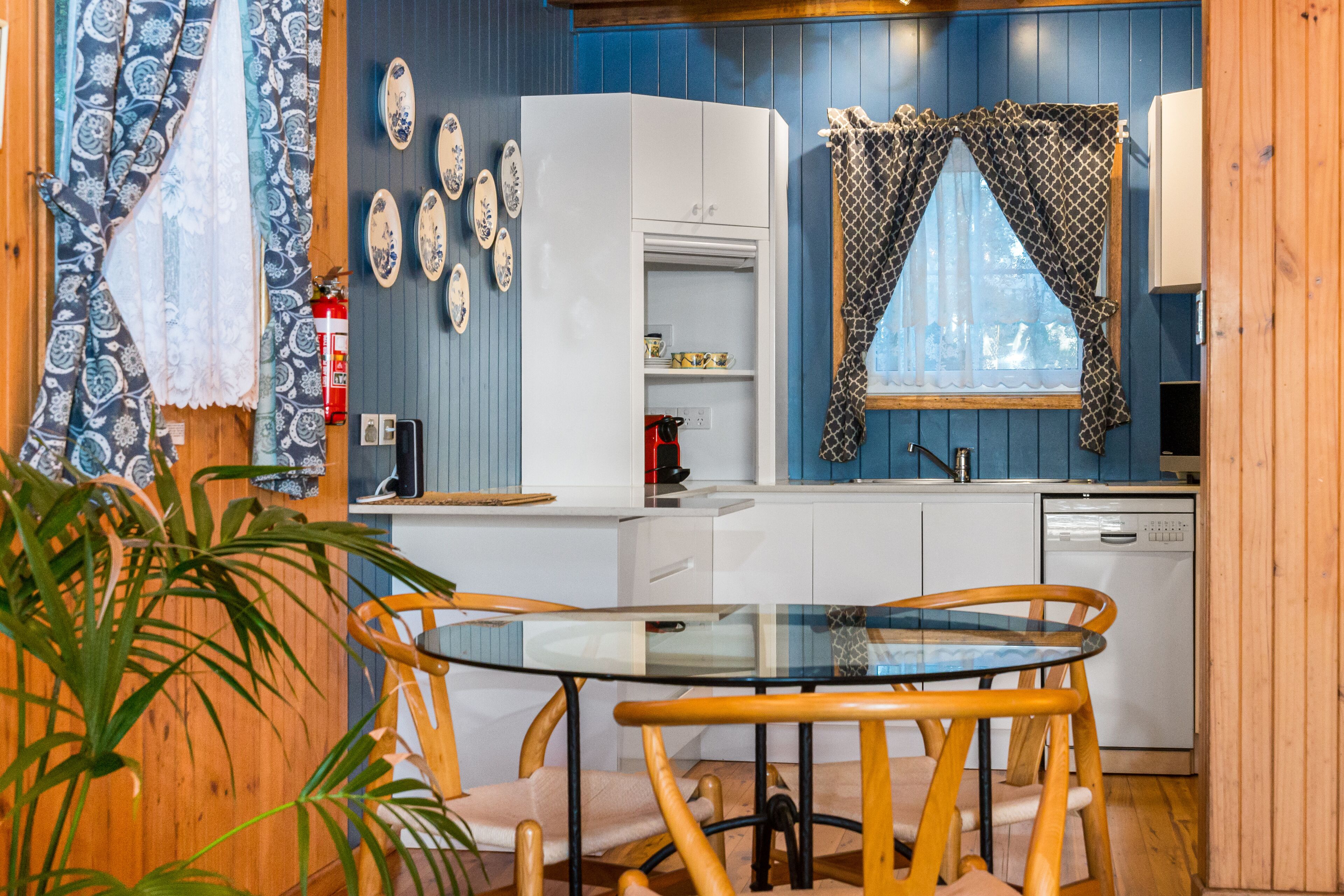 A compact kitchen with white cabinets, a glass table, and wooden chairs.