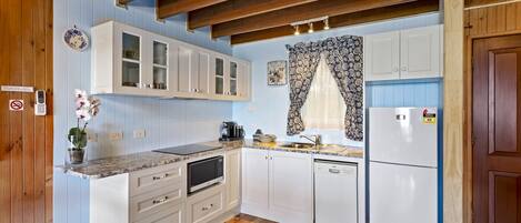 Una cocina con vigas de madera, armarios blancos, microondas, cafetera y refrigerador.