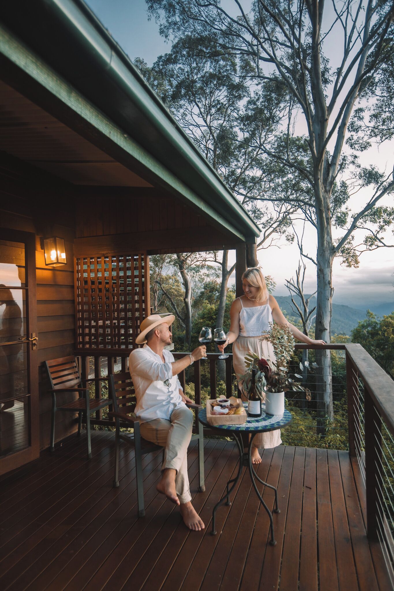 A wooden deck with a table and chairs, overlooking a scenic landscape with trees and mountains.